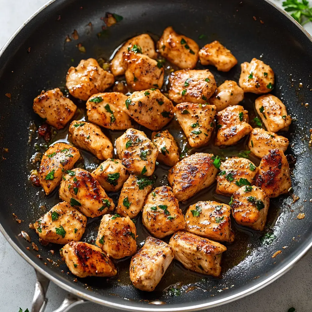 Trozos de pollo cocinados y dorados, adornados con perejil en una sartén.