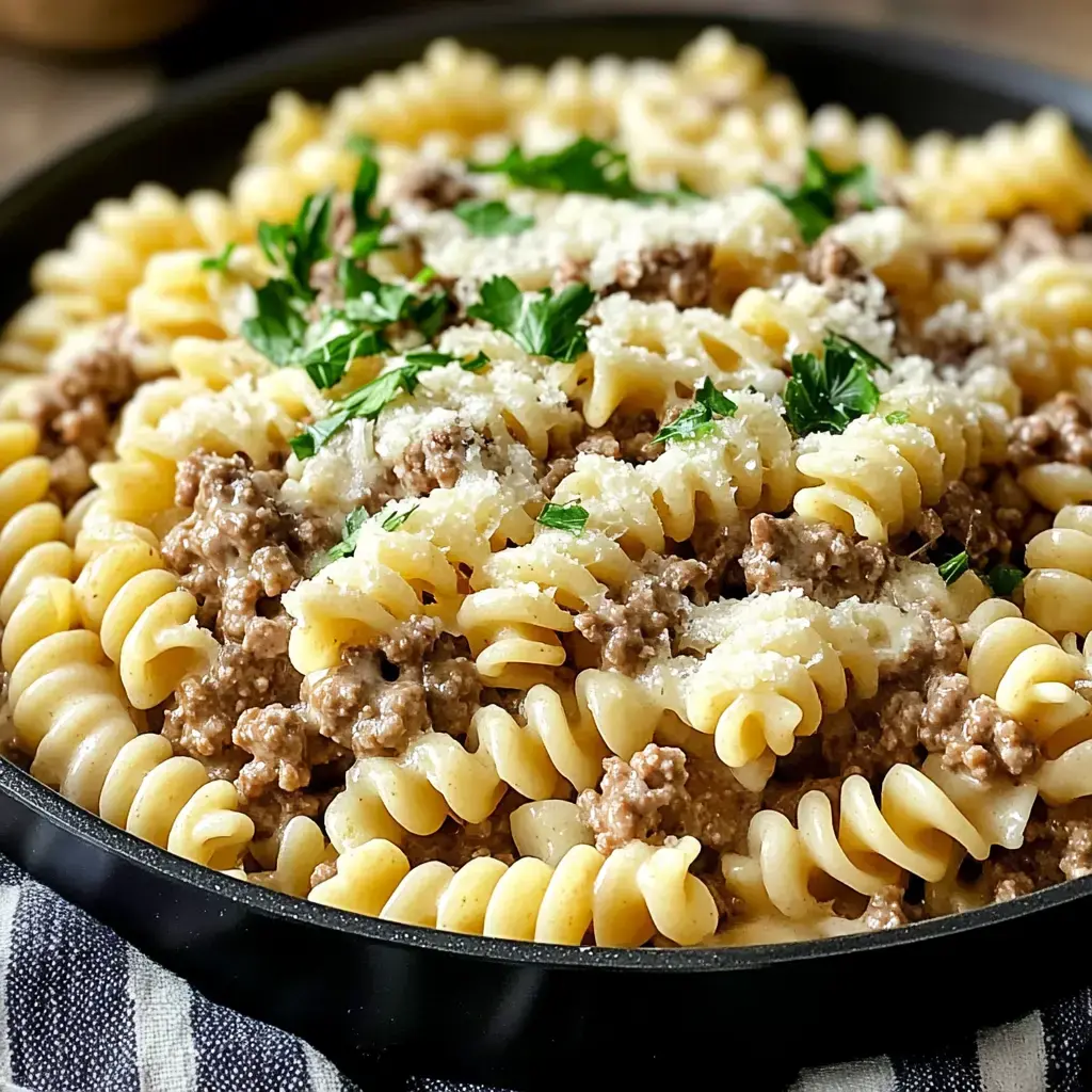 Un primer plano de un plato con pasta rotini cubierta con carne molida sazonada, perejil y queso rallado.