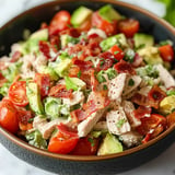 Un tazón de ensalada de pollo con tocino y tomates.